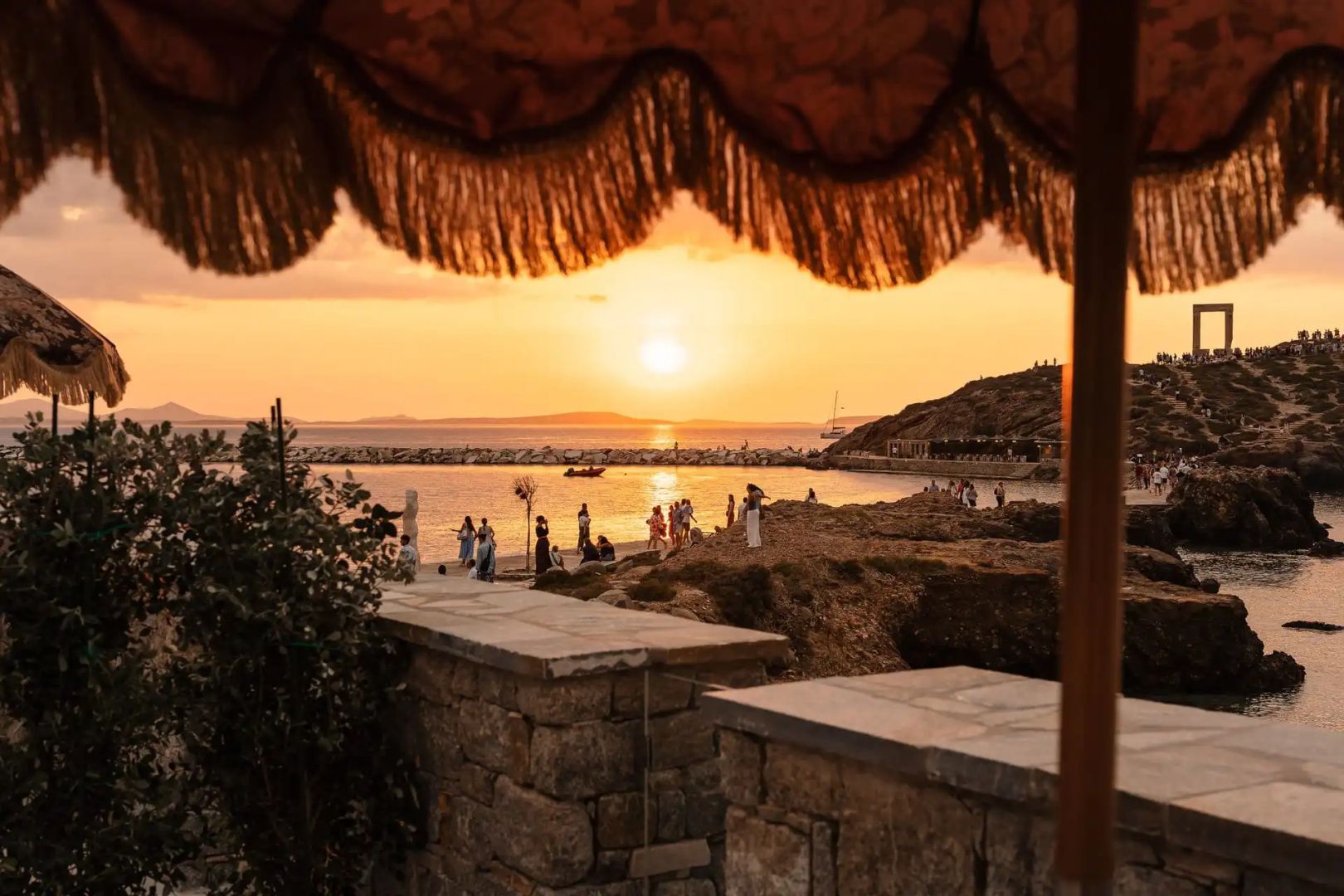 Blick auf das Meer und eine Küstenlandschaft bei Sonnenuntergang unter einem Sonnenschirm.