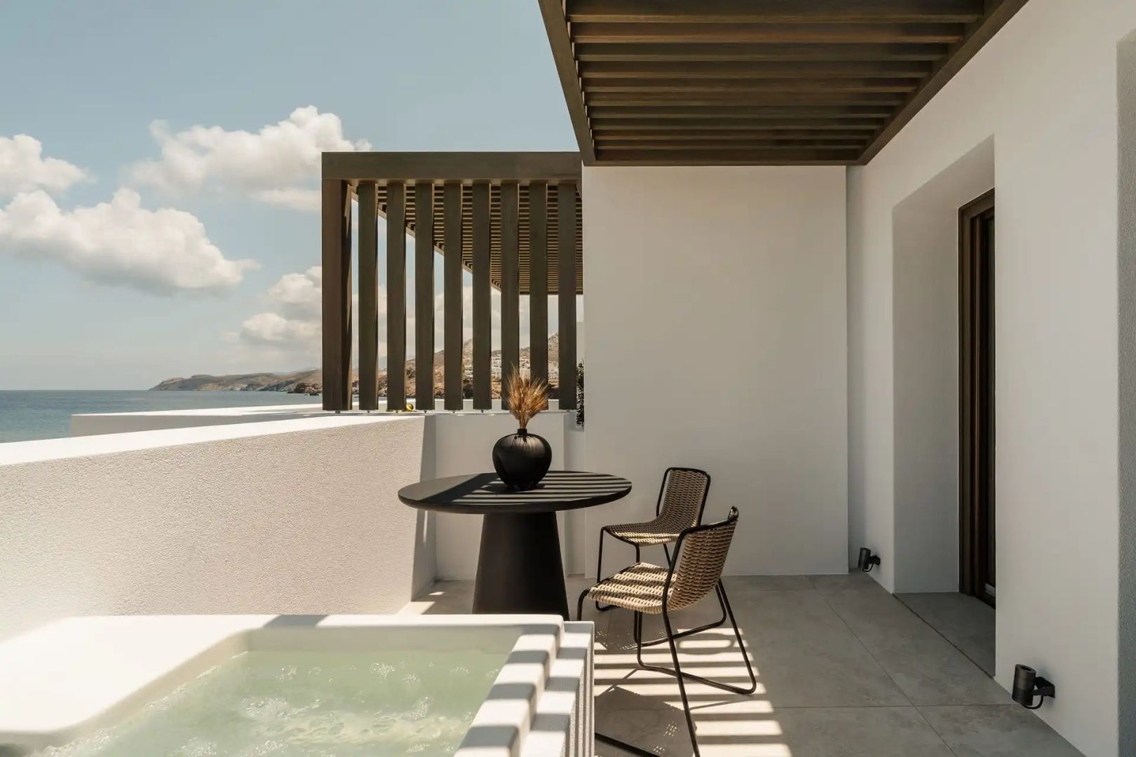 Terrasse mit integriertem Whirlpool, dunklem Esstisch, Stühlen und Blick auf das Meer.