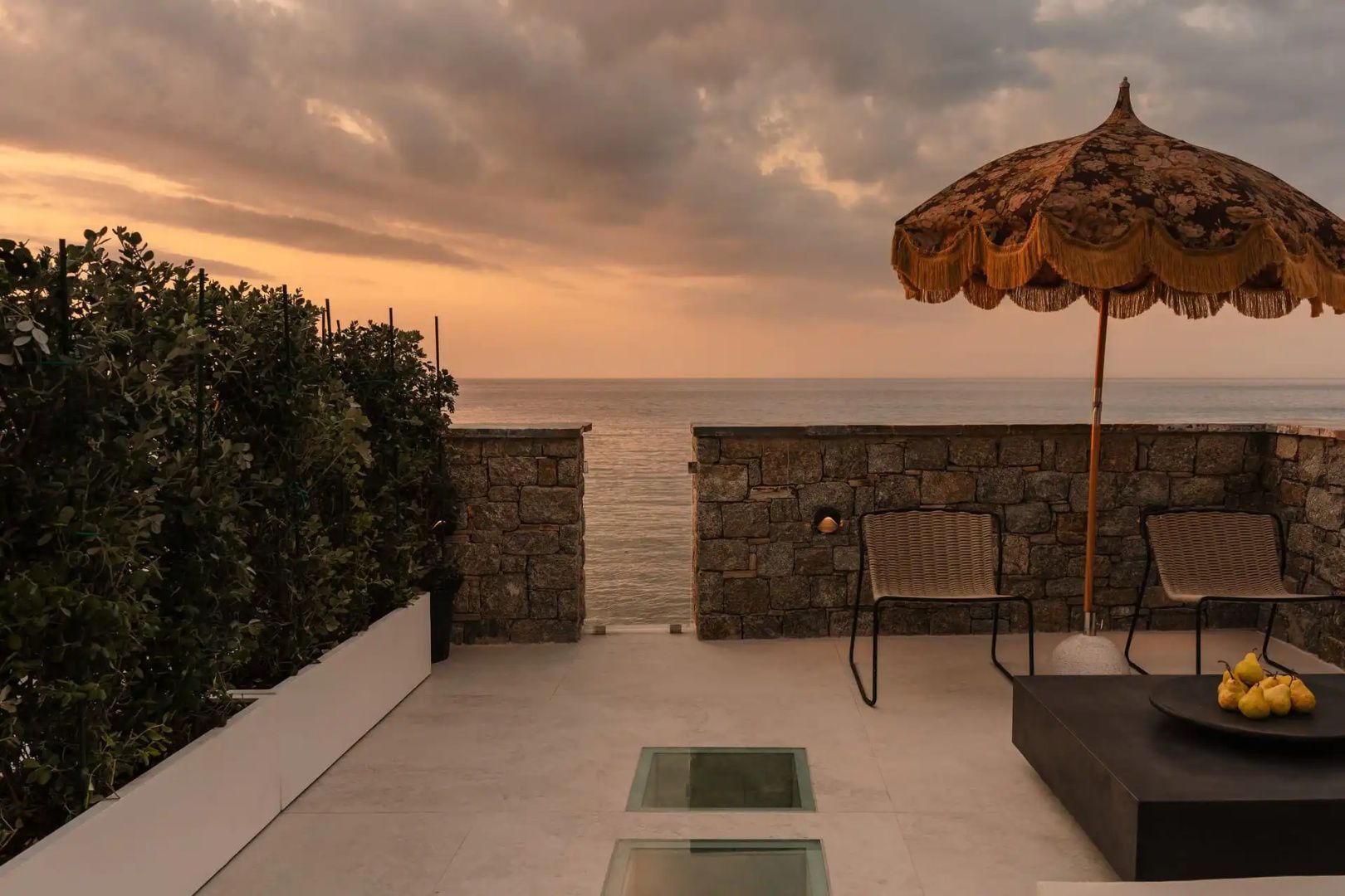Terrasse mit Steinmauer, Stuhl und Sonnenschirm mit direktem Blick auf das offene Meer.