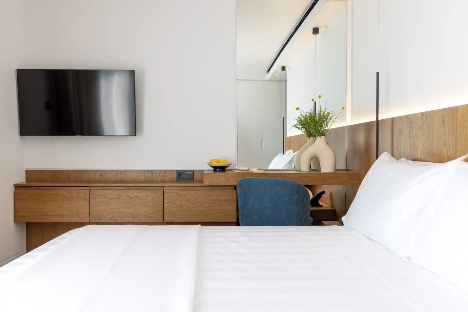 Helles Hotelzimmer mit Doppelbett, Flachbildfernseher und Holzschreibtisch mit Stuhl.