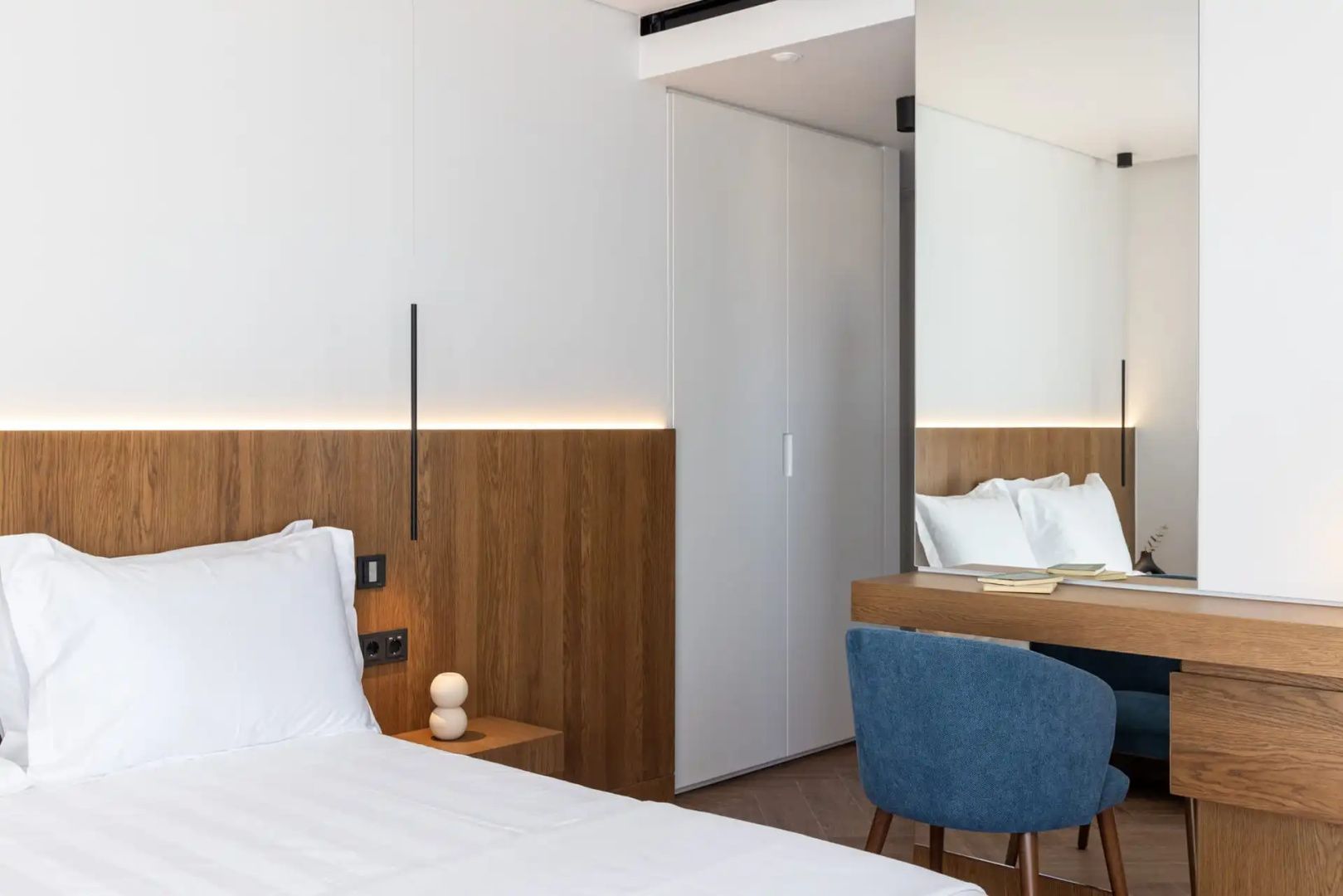 Helles Hotelzimmer mit großem Bett, Holzpaneel, blauem Sessel und Schminktisch.