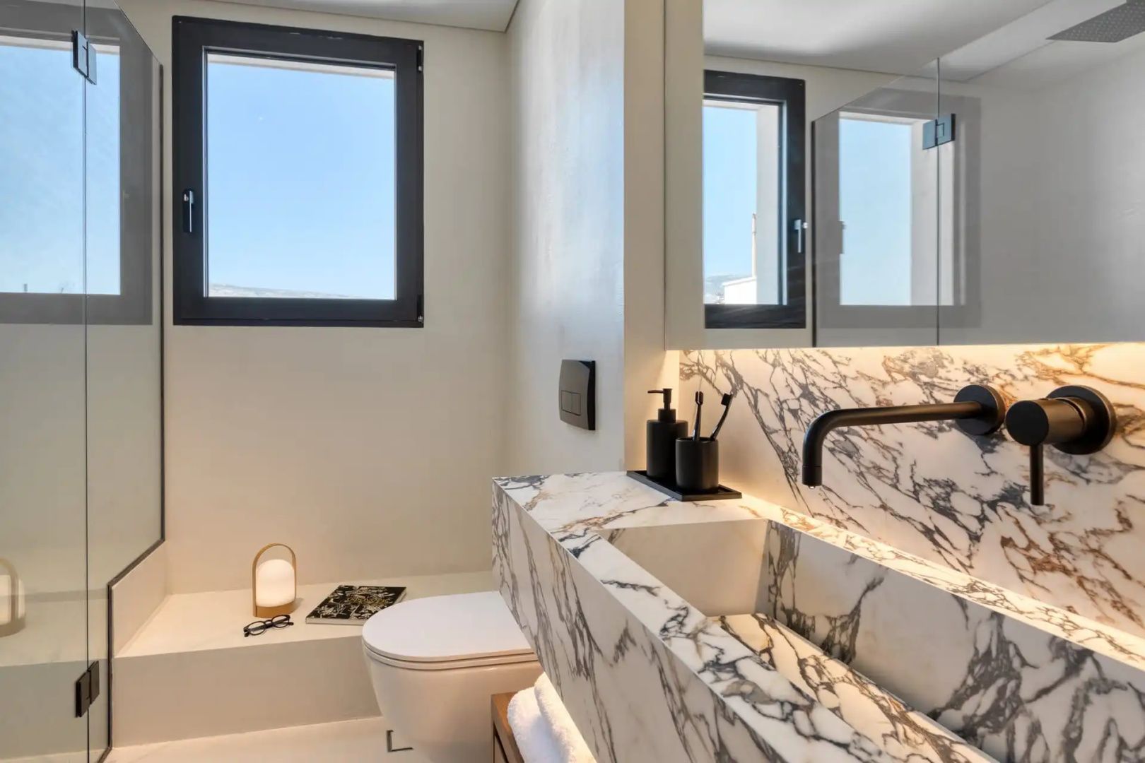 Badezimmer mit marmoriertem Waschtisch, schwarzer Armatur, Toilette und Fenster.