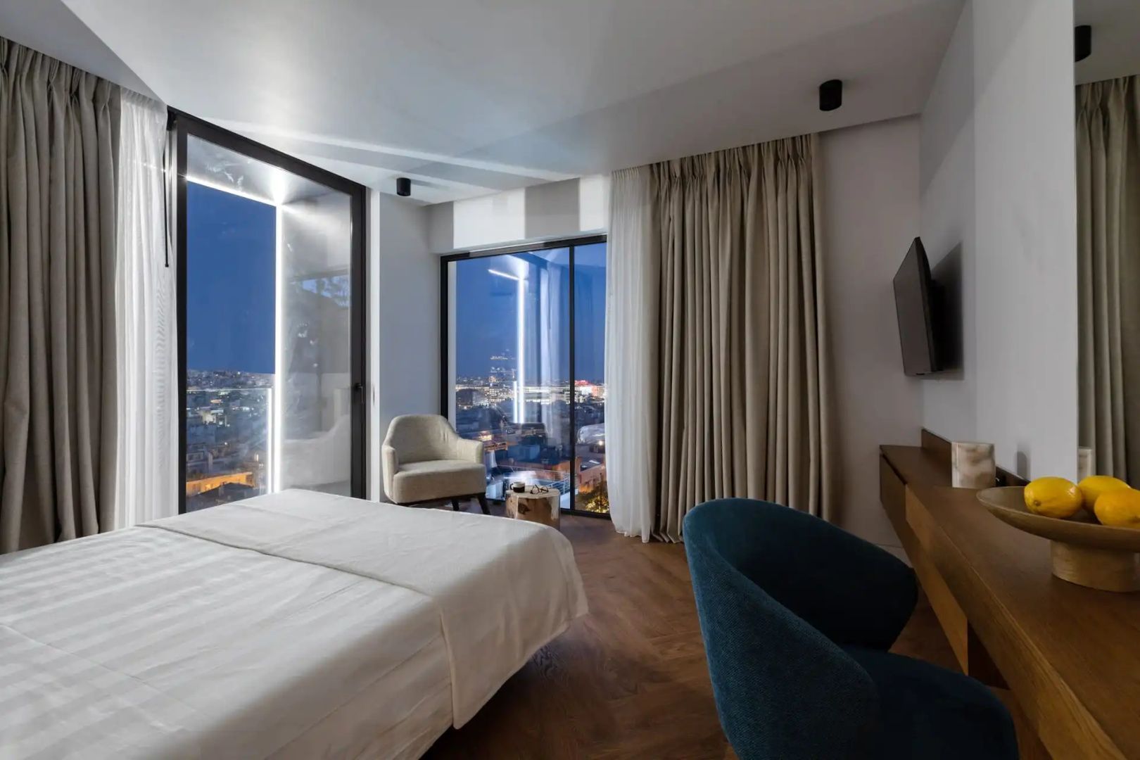 Hotelzimmer am Abend mit Blick durch Panoramafenster auf die beleuchtete Stadt.