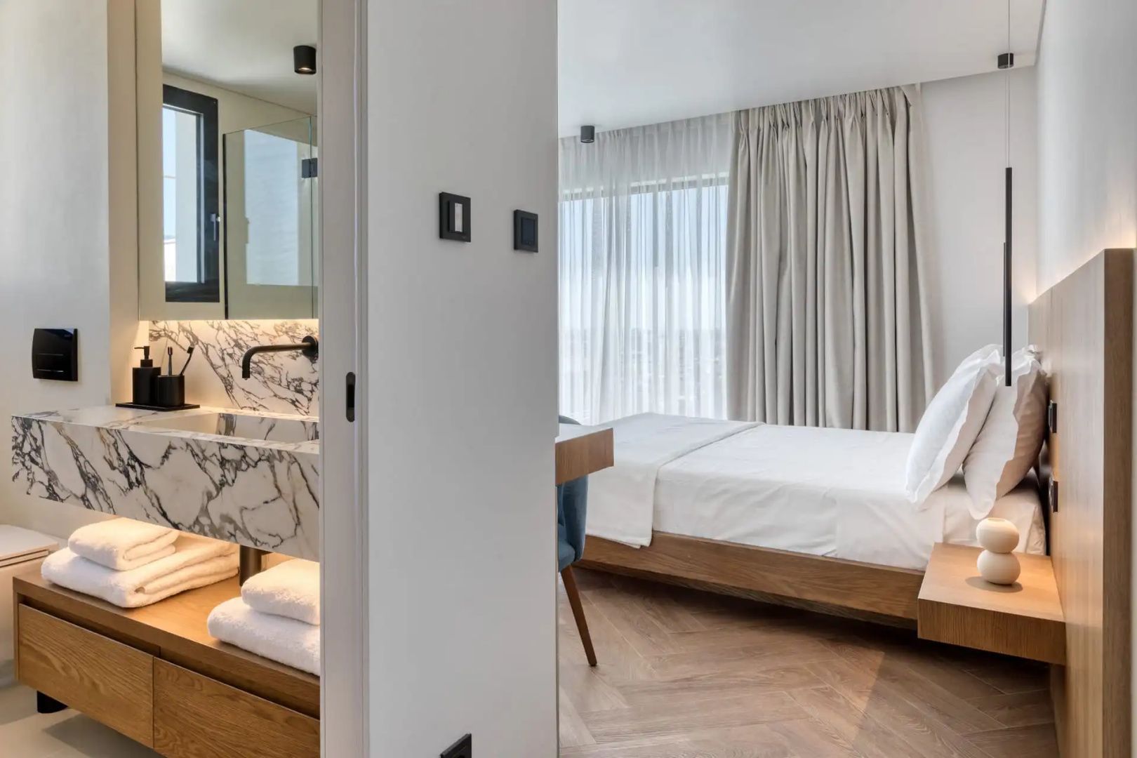 Blick in ein modernes Hotelzimmer mit Doppelbett, Holzboden und Marmorwaschtisch im Vordergrund.