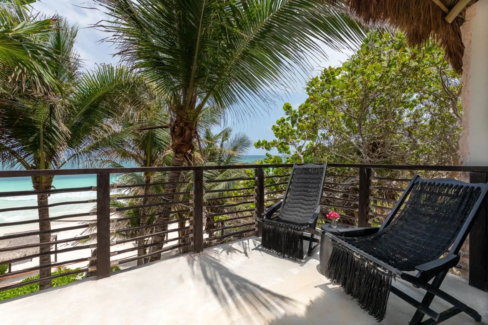 Balkon mit zwei schwarzen Stühlen, umgeben von Palmen und Blick auf das Meer.