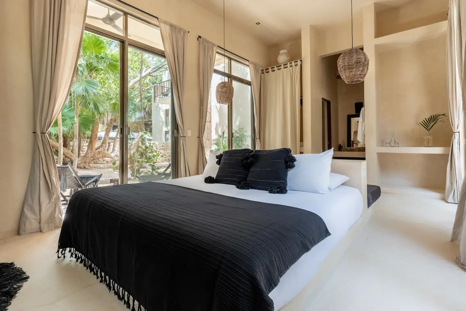 Doppelbett mit schwarzer Decke und Kissen vor großen Glasfronten im Hotelzimmer.