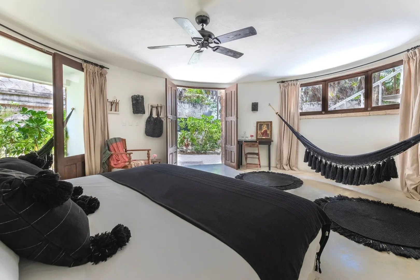 Schlafzimmer mit großem Bett, schwarzer Decke, Deckenventilator und Tür zum Garten.