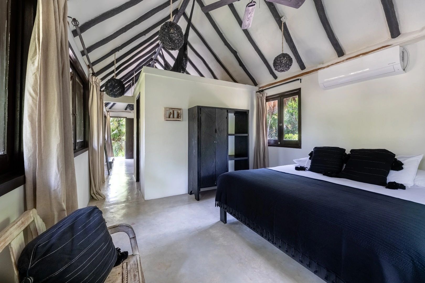 Helles Zimmer mit hohem Spitzdach aus Holz, einem Bett mit schwarzer Decke und dunklem Schrank.