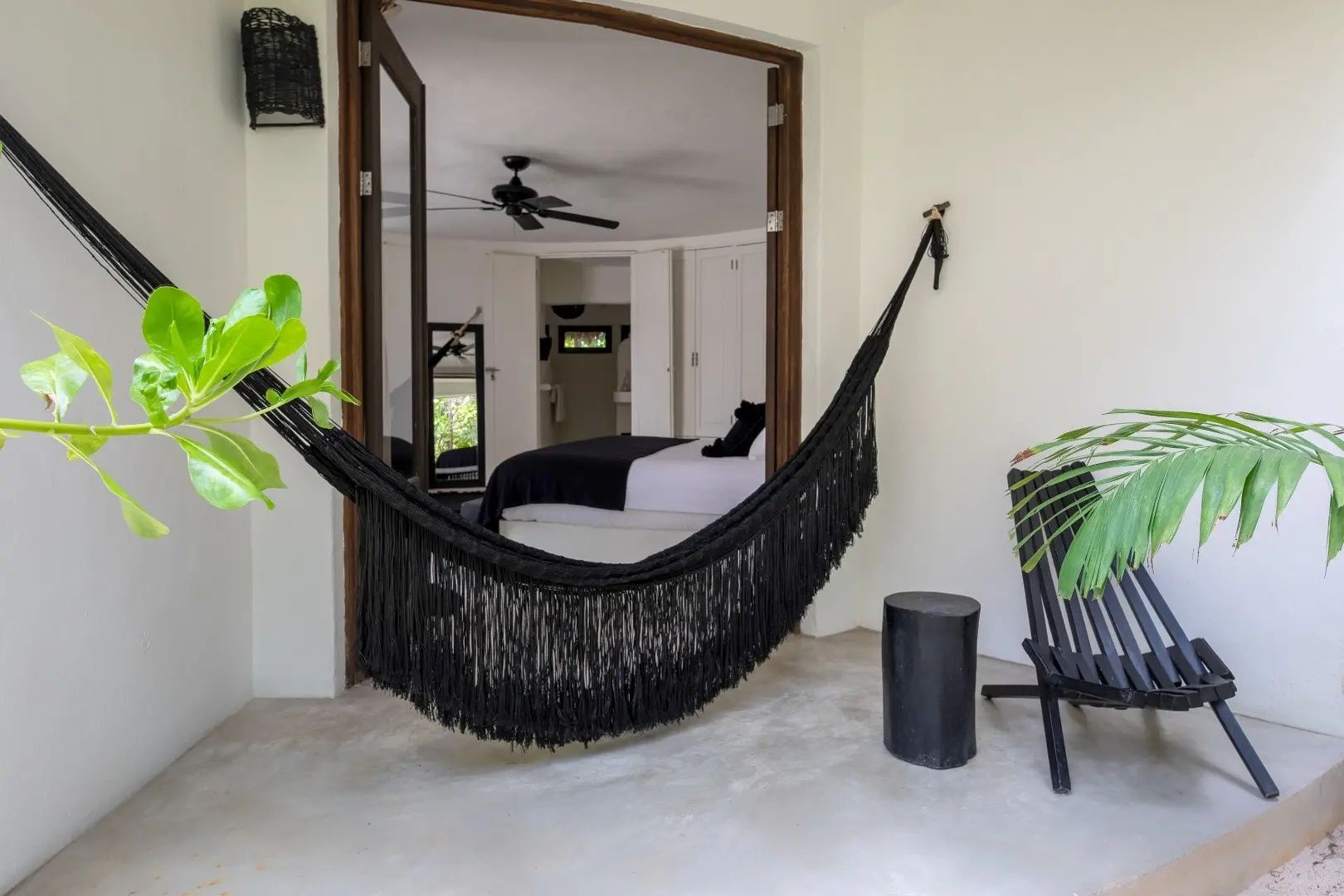 Überdachte Terrasse mit schwarzer Hängematte und Blick durch die Tür in das Schlafzimmer.