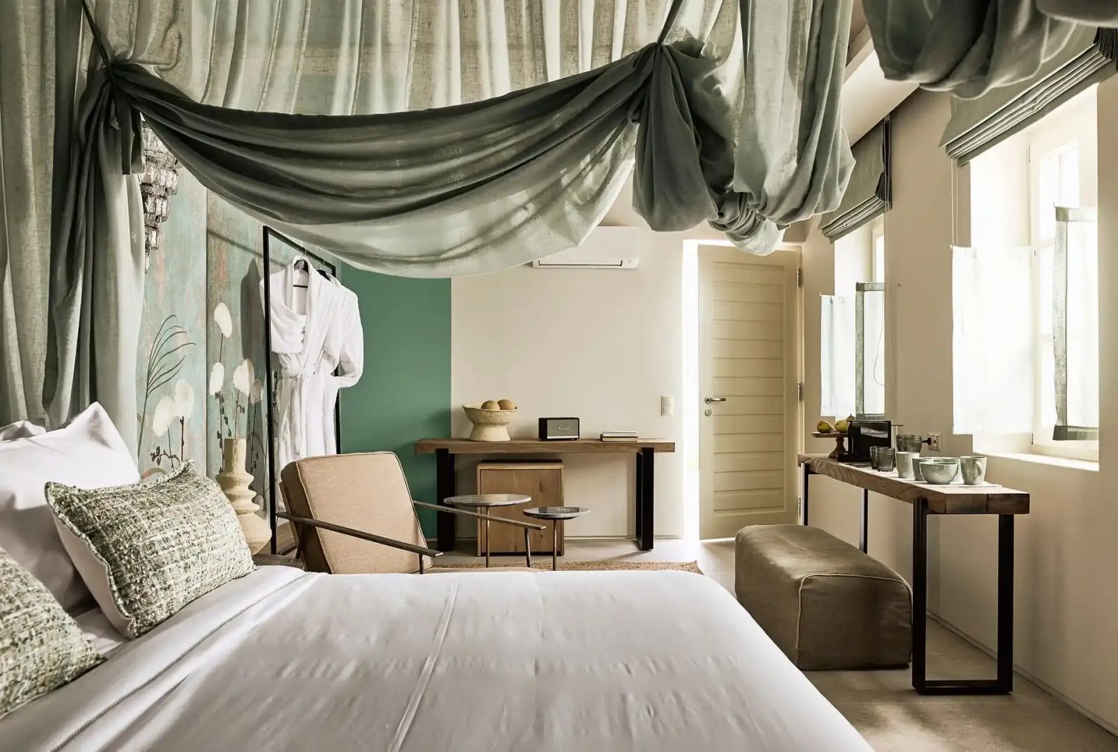 Schlafzimmer einer Suite mit Himmelbett, Holzmöbeln und einem Sessel.