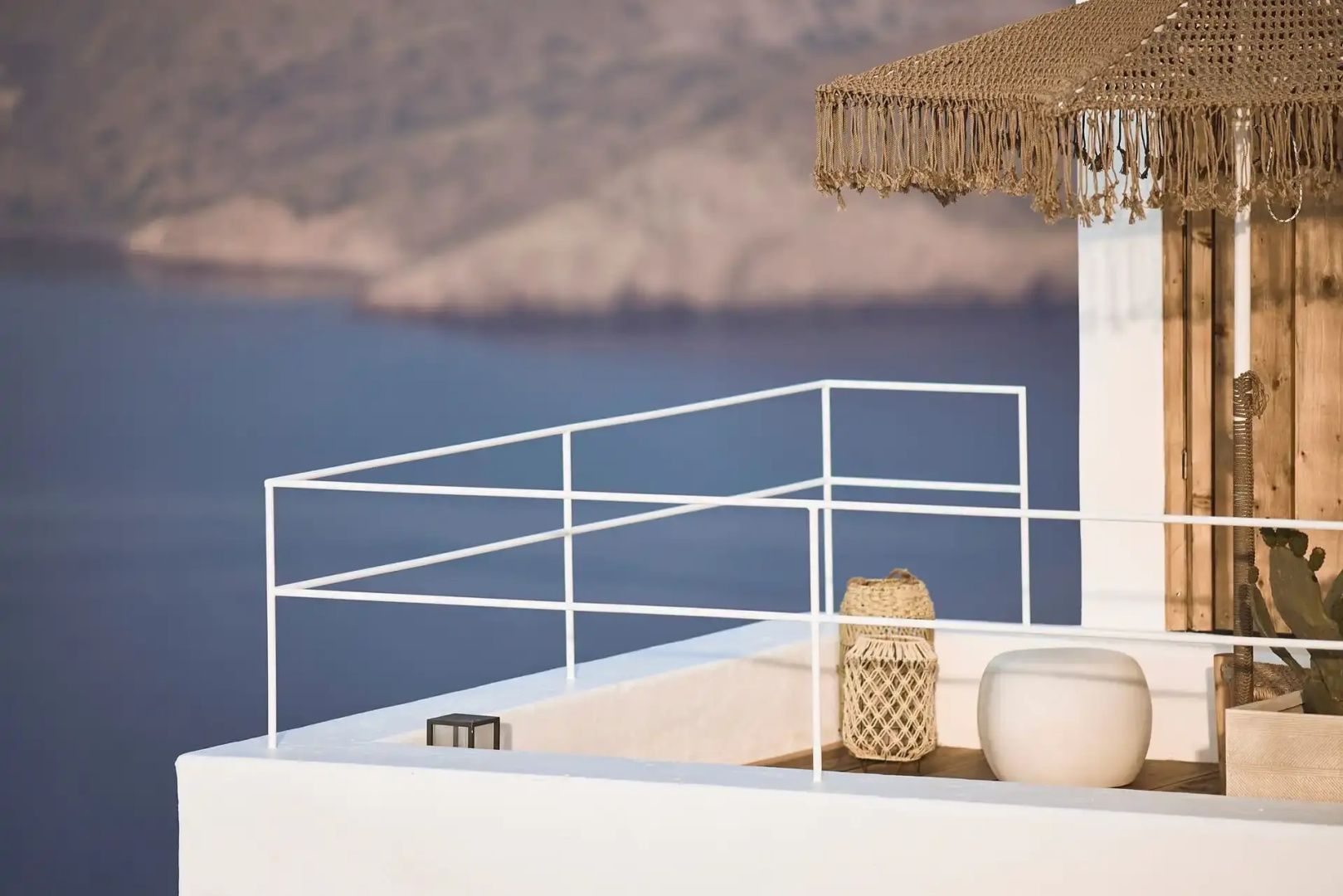 Weißes Geländer einer Terrasse mit Blick auf das Meer und gegenüberliegende Hügel.