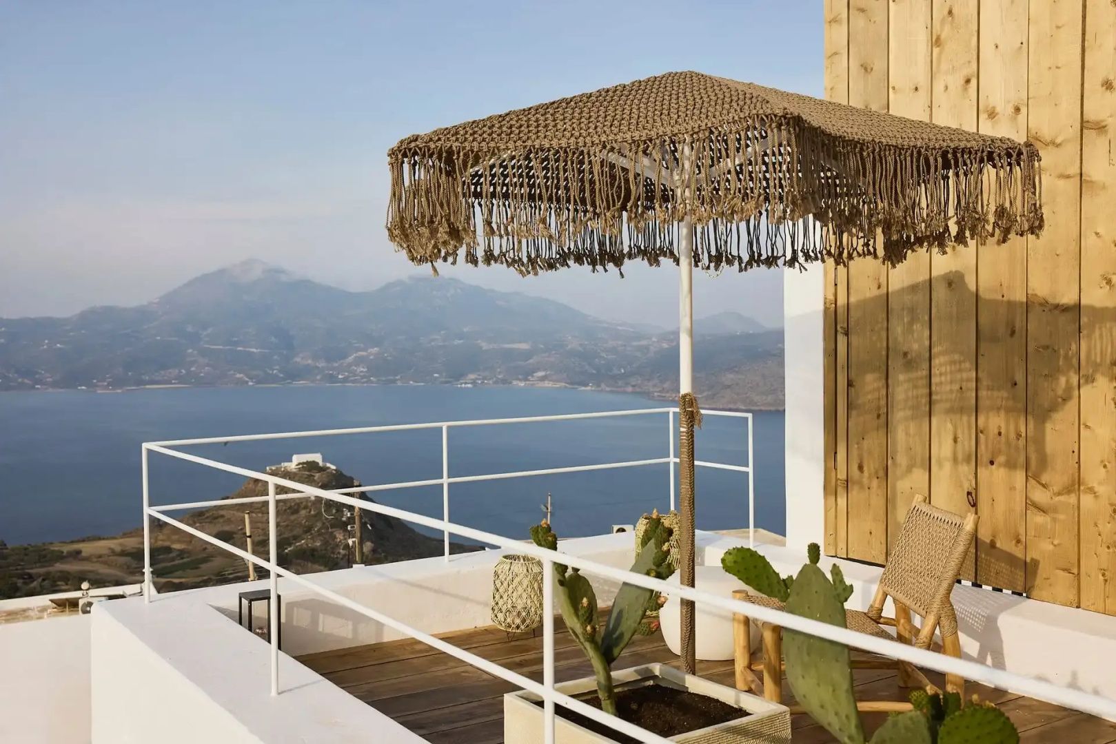 Terrasse mit gehäkeltem Sonnenschirm und Blick auf das blaue Meer sowie die hügelige Küste.