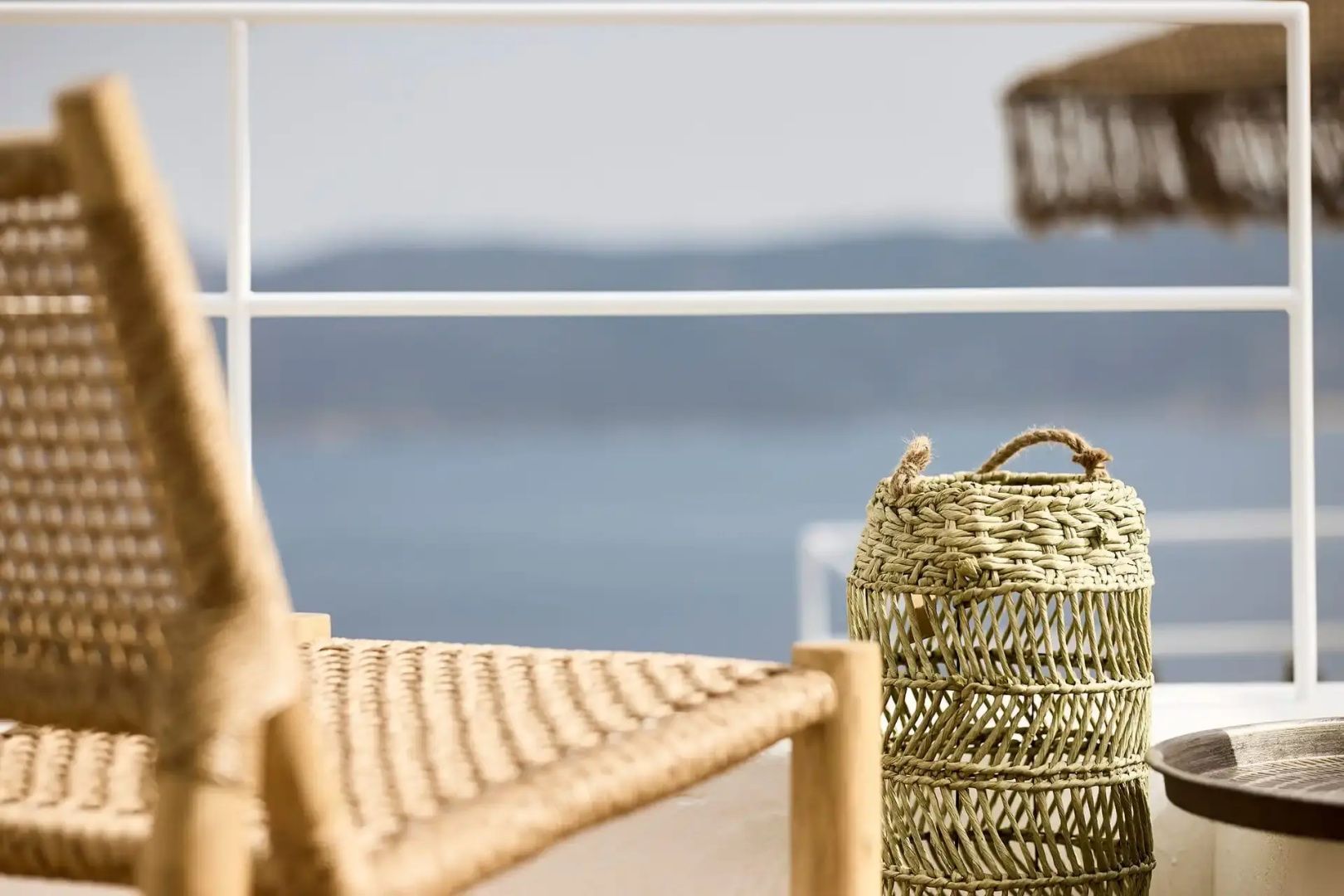 Terrasse mit Flechtstuhl und Blick auf das Meer sowie die umliegende Küstenlandschaft.