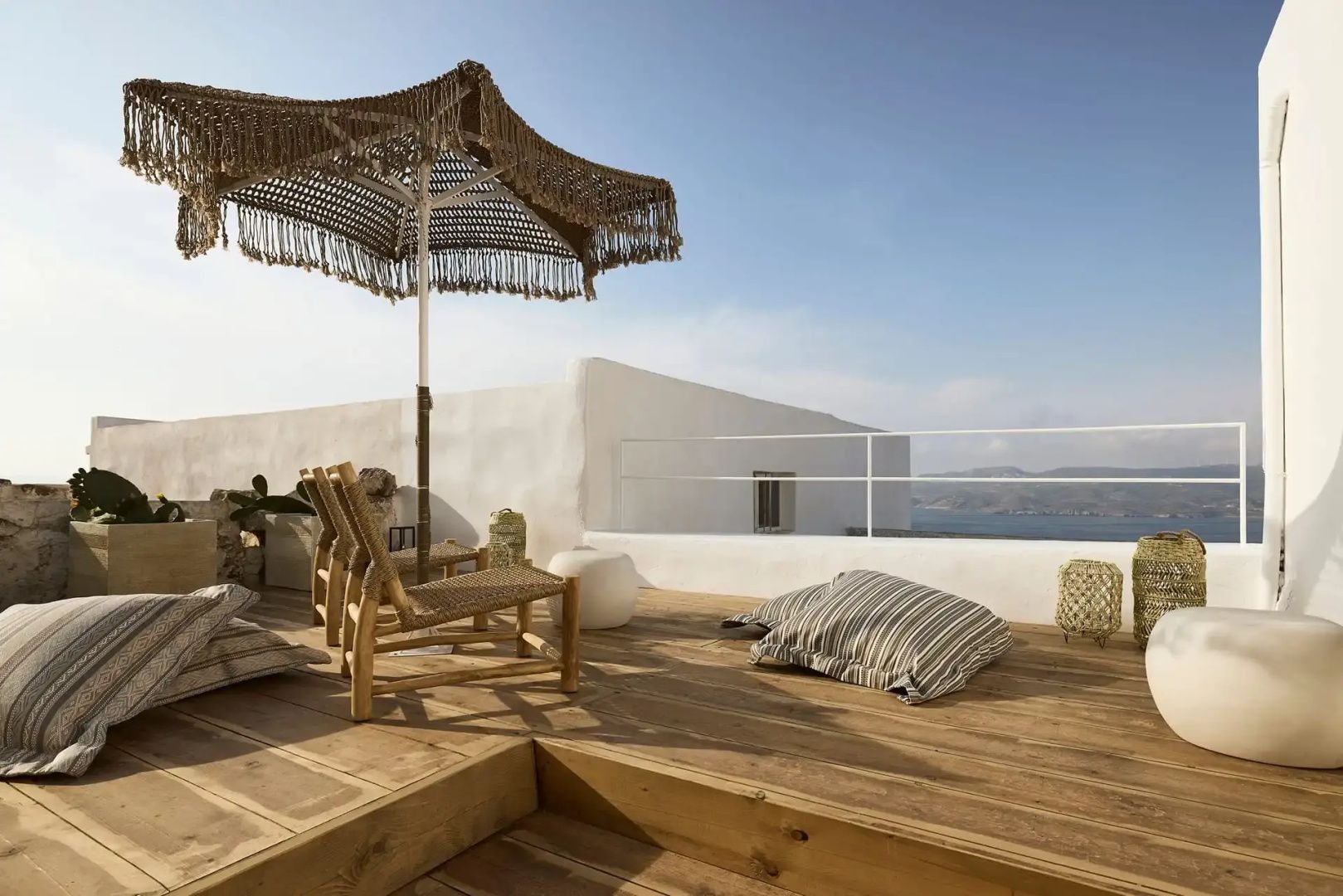 Sonnenterrasse aus Holz mit Sonnenschirm, Holzstühlen und Blick auf das Meer.