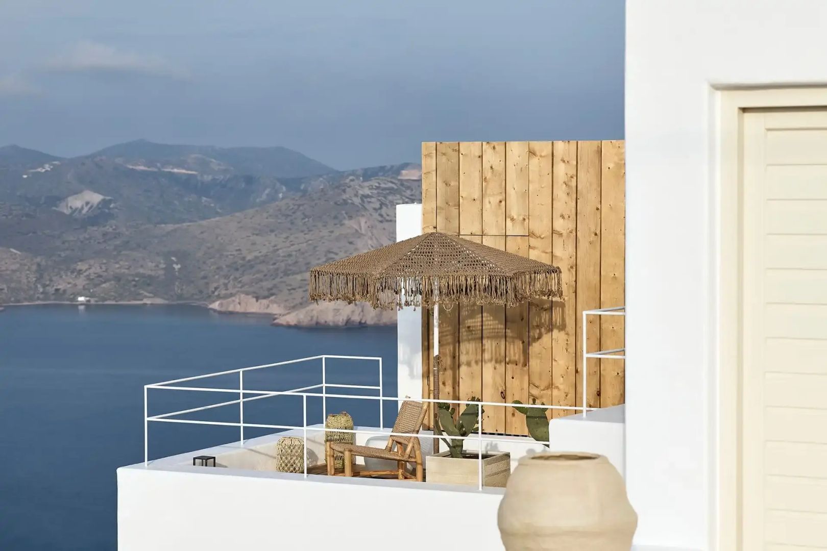 Sonnige Dachterrasse mit Sonnenschirm, Sitzgelegenheiten und Panoramablick auf das Meer.