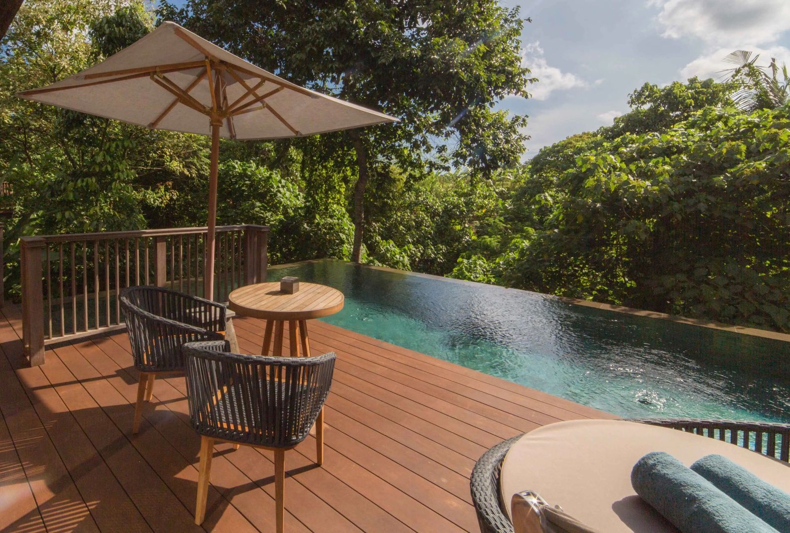 Terrasse mit Holzdeck, Sitzgelegenheiten, Sonnenschirm und einem Pool am Waldrand.