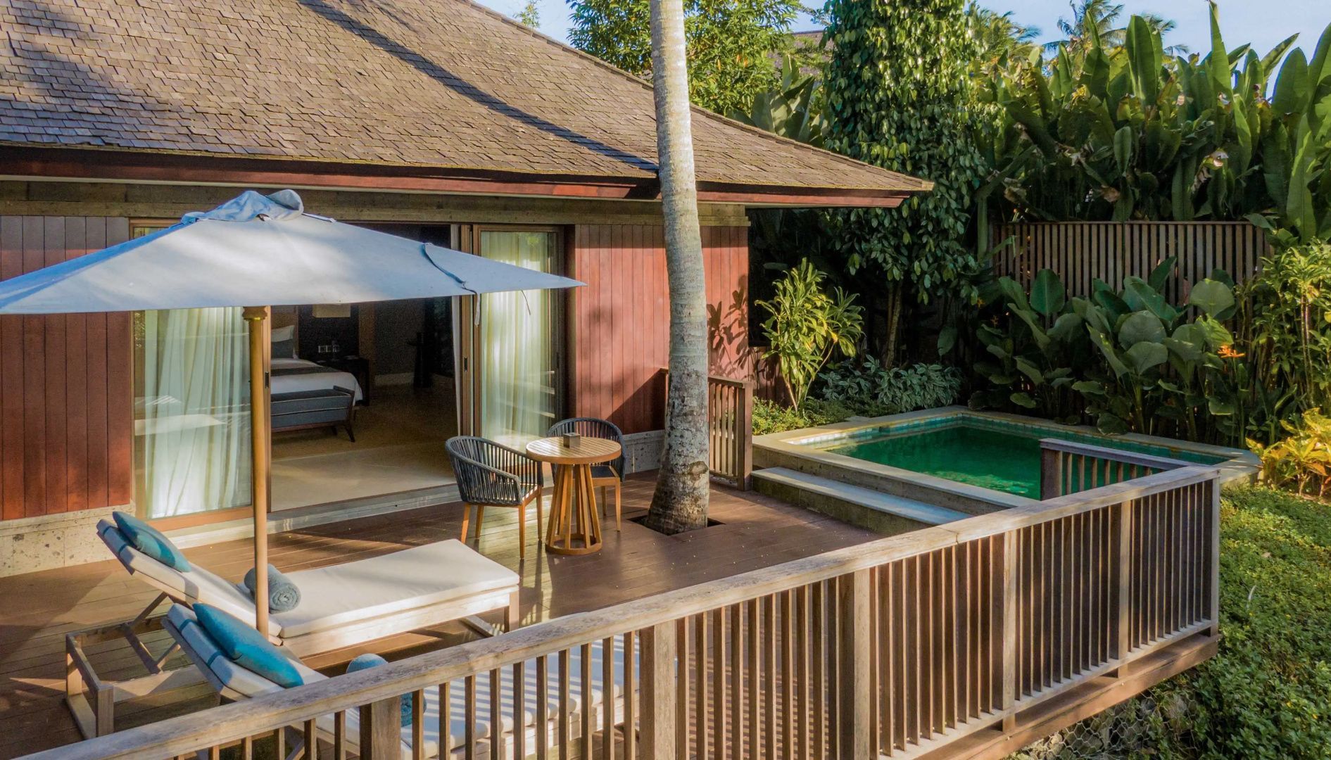 Holzterrasse einer Villa mit Sitzbereich, Sonnenschirm und kleinem Pool.