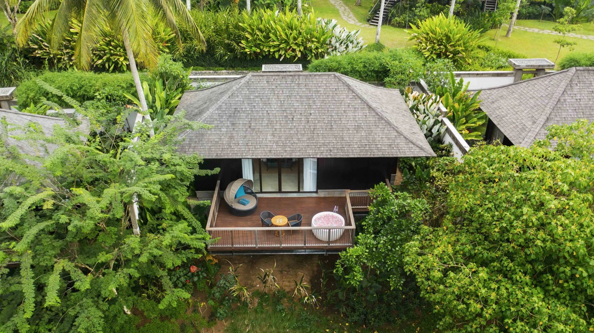 Holzvilla mit Terrasse, Sitzmöglichkeiten und Outdoor Wanne umgeben von tropischem Grün.