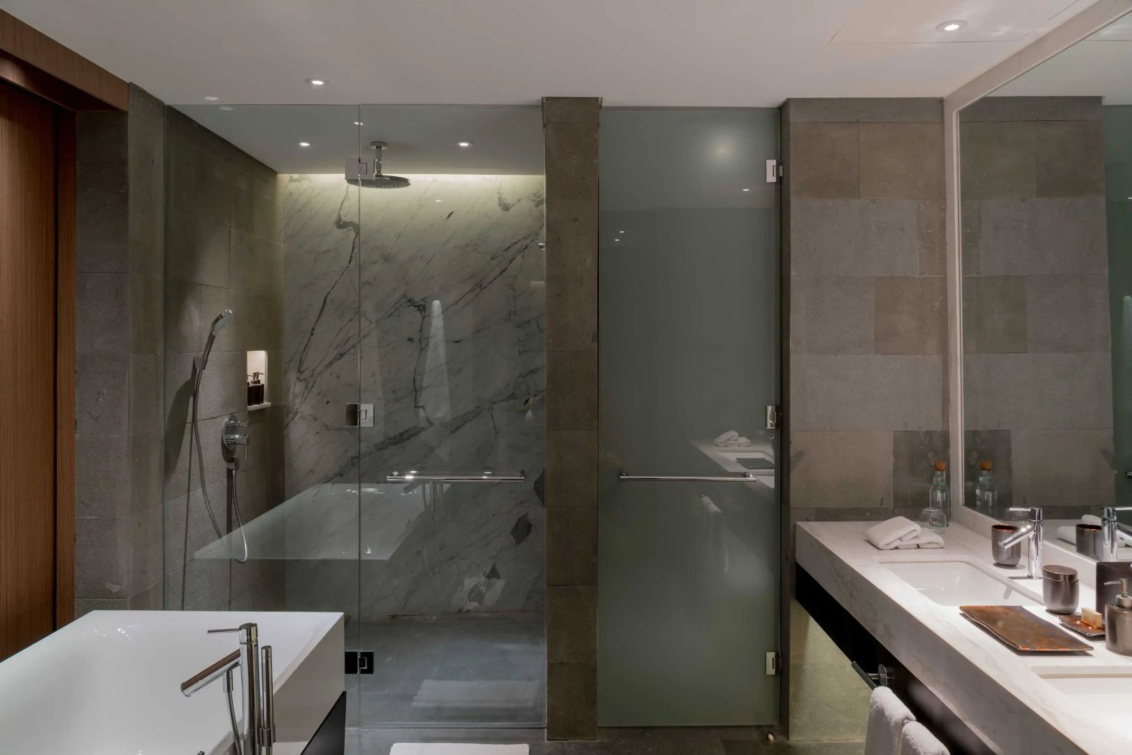 Badezimmer mit ebenerdiger Glasdusche und Waschtisch aus Naturstein.