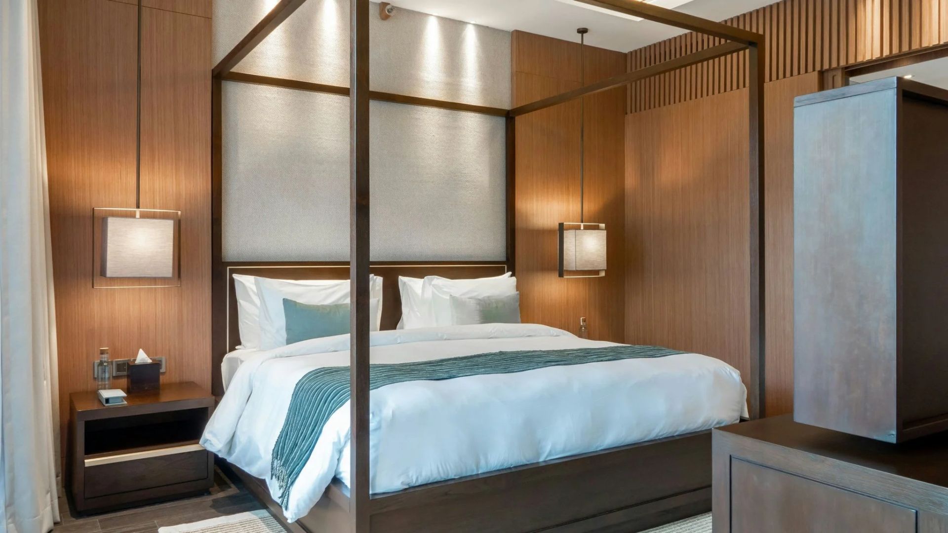 Großes Himmelbett aus Holz mit weißer Bettwäsche und stilvoller Beleuchtung.