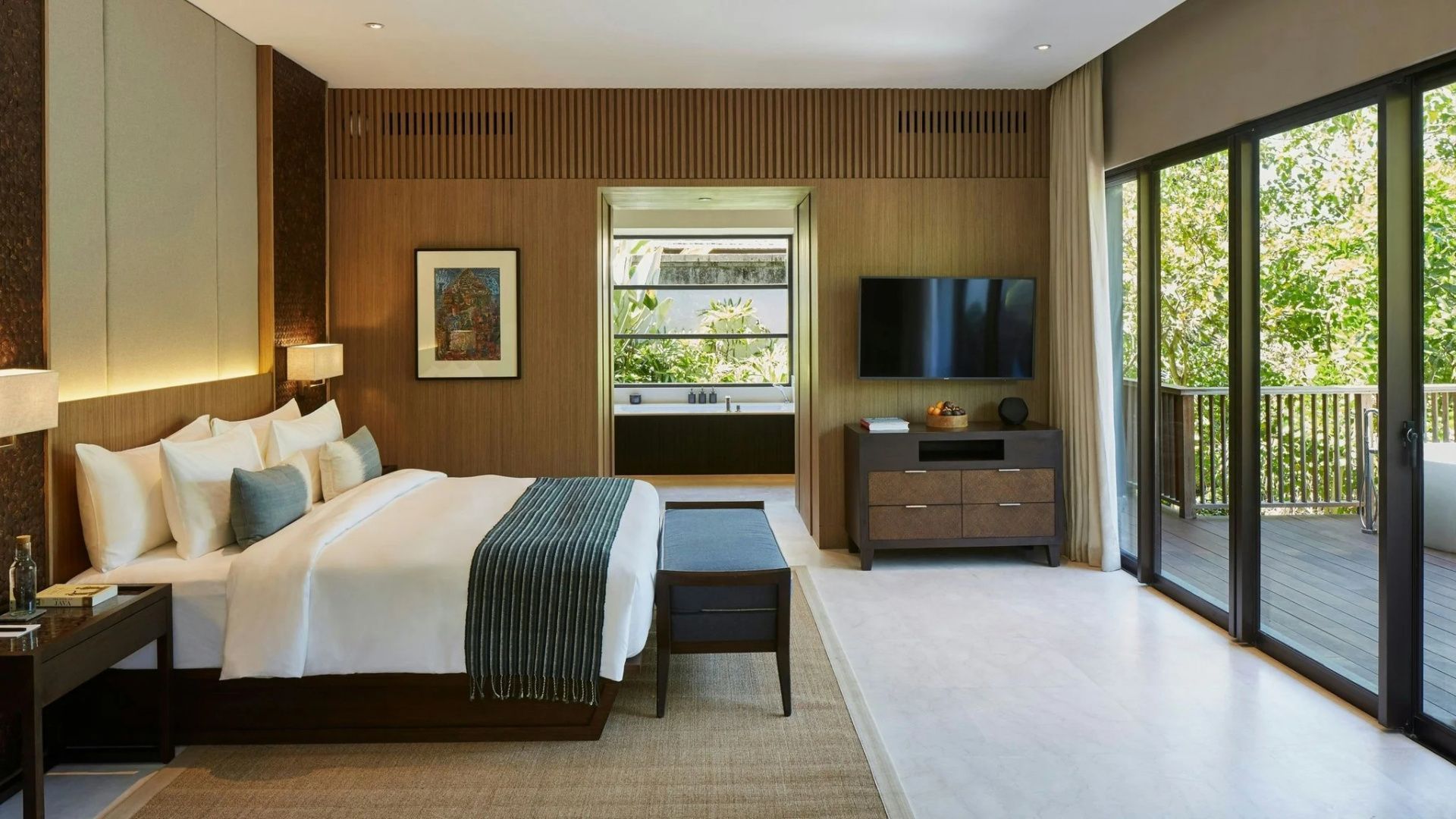 Modern eingerichtetes Schlafzimmer mit Doppelbett, Fernseher und Blick ins Badezimmer.