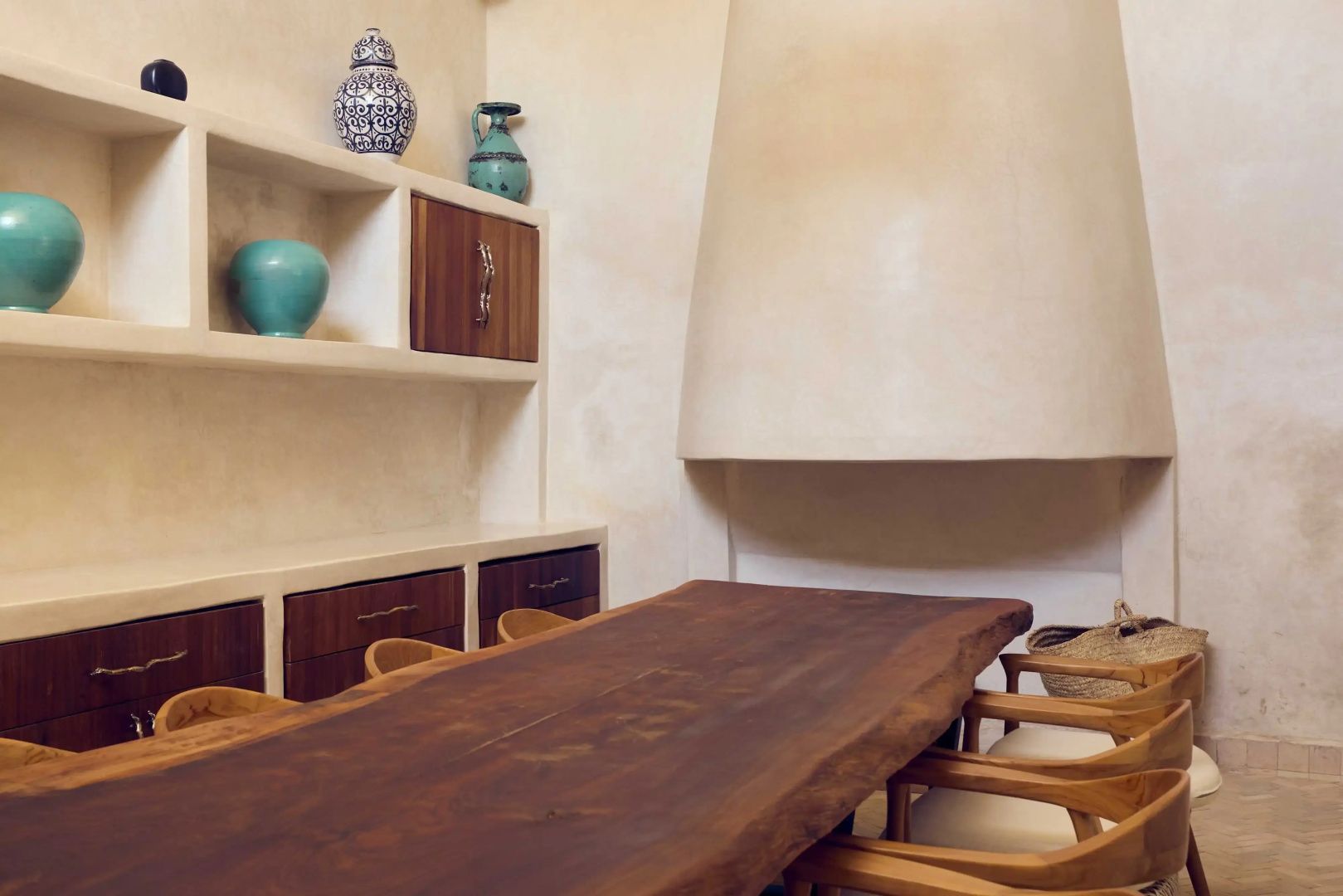 Rustikaler Holztisch mit Holzstühlen vor einer hellen Wand mit Regalen und Tongefäßen.