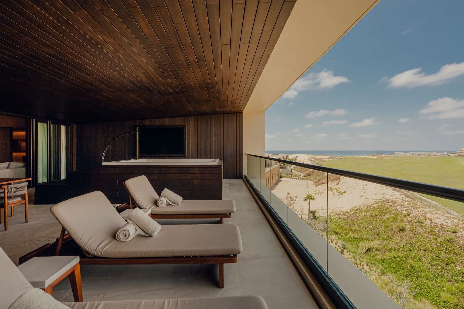 Überdachte Terrasse mit zwei Liegestühlen, Whirlpool und Ausblick auf das Meer.