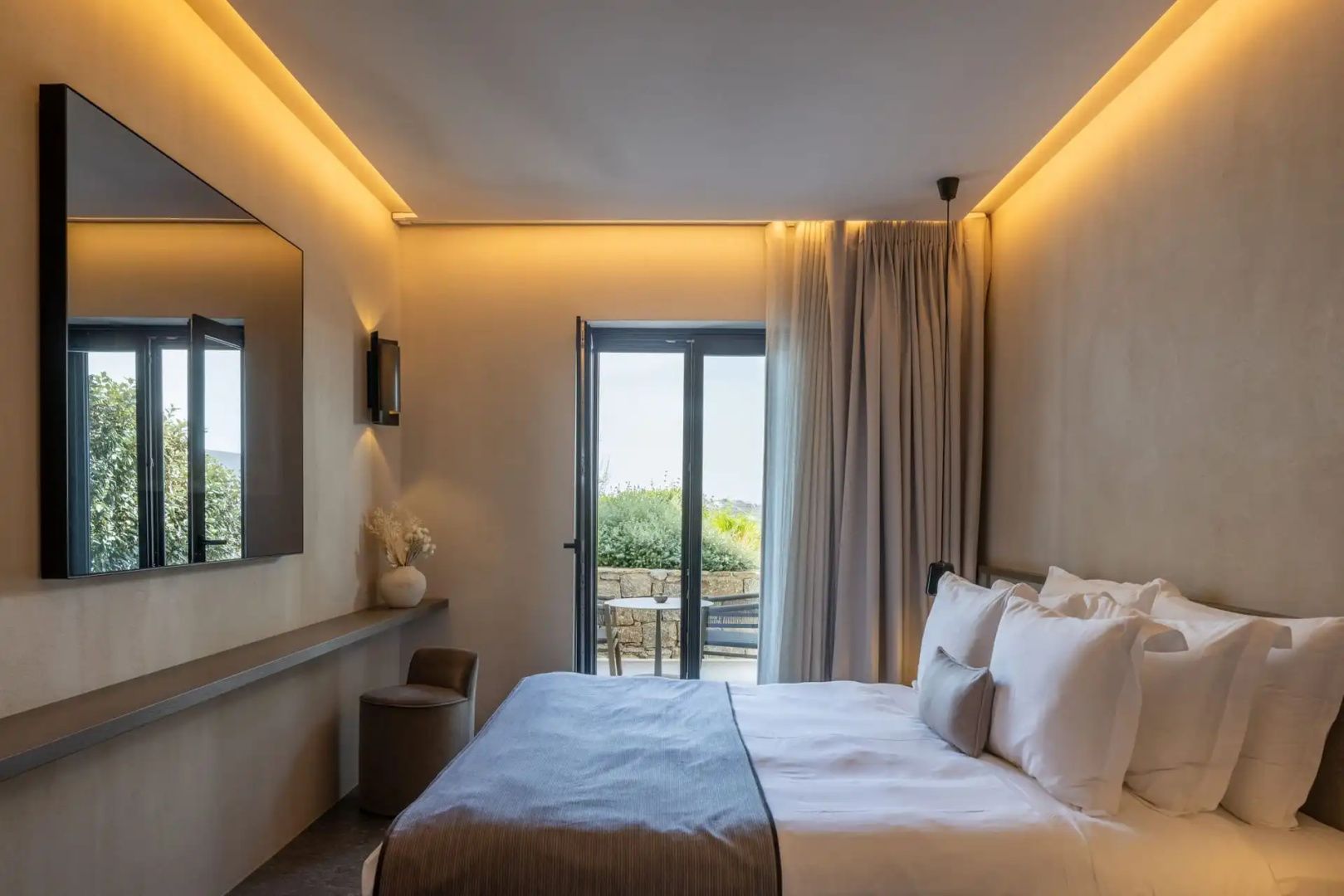 Modernes Hotelzimmer mit Doppelbett, indirekter Deckenbeleuchtung und Zugang zur Terrasse.