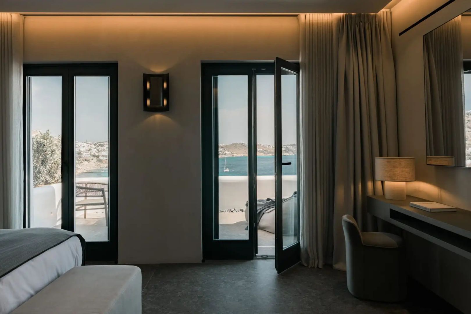 Blick durch geöffnete Balkontür auf das Meer und die Küste von Mykonos.
