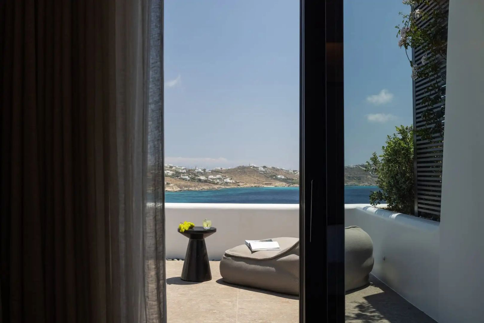 Blick durch ein Fenster auf eine Terrasse mit Sitzsack und Meeresaussicht.