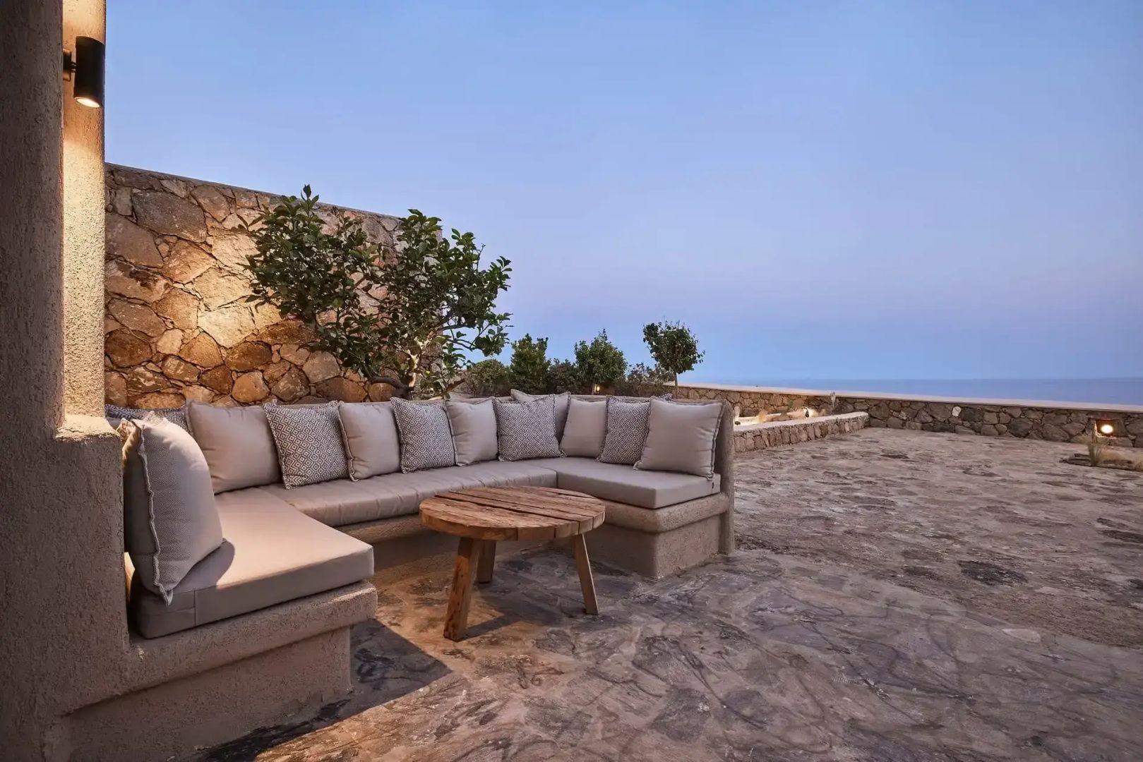 Sitzbereich auf einer Terrasse mit Holzbeistelltisch und freiem Blick auf das Meer.