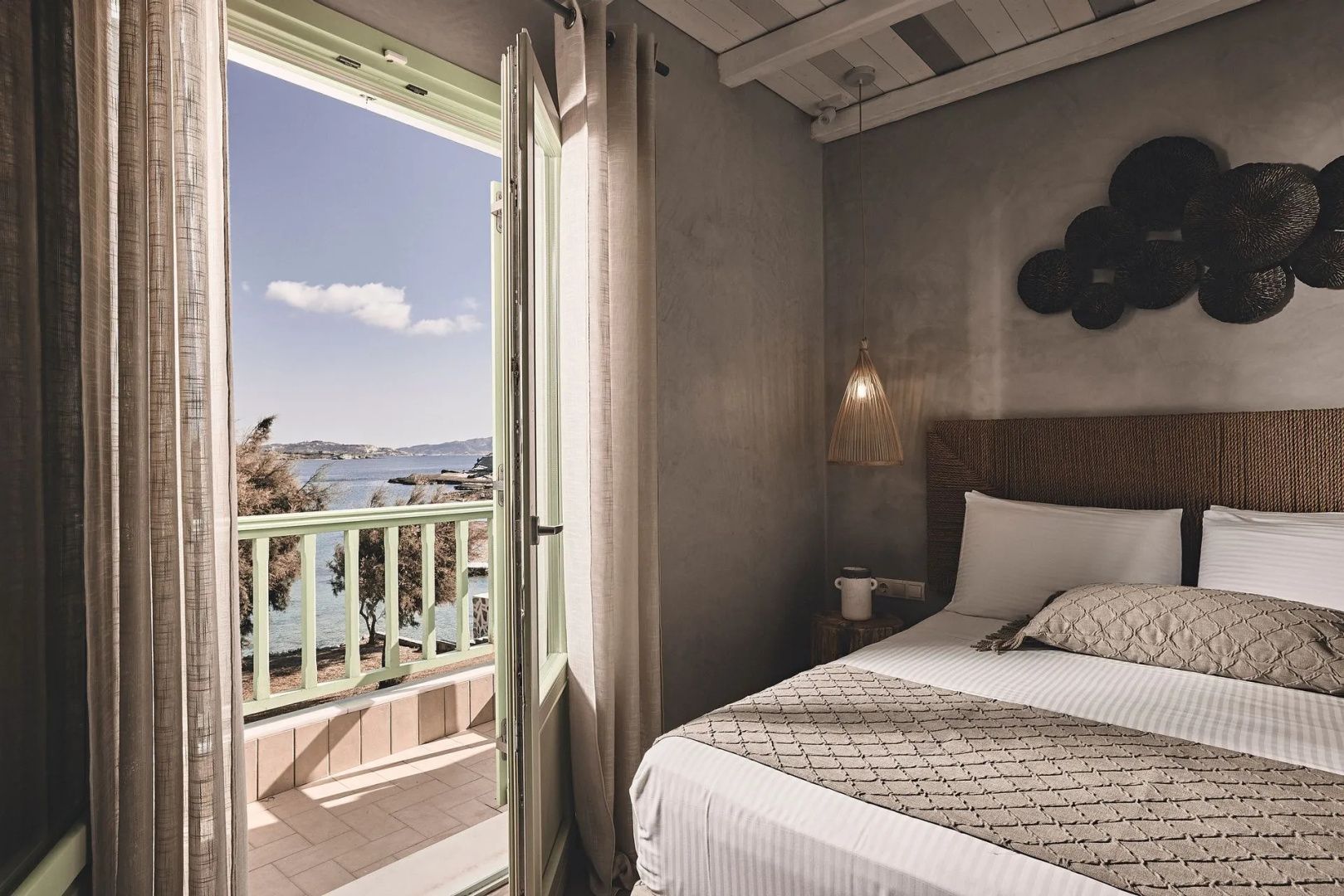 Blick durch die geöffnete Balkontür auf das Meer und die Küstenlandschaft vom Schlafzimmer aus.