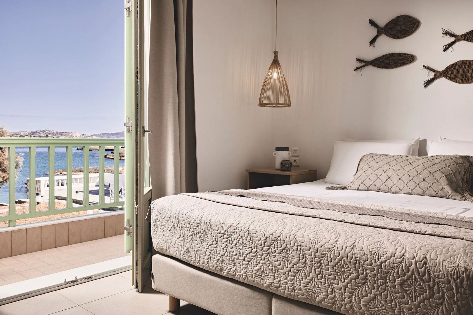 Schlafbereich mit Doppelbett und geöffneter Balkontür mit Blick auf das Meer.