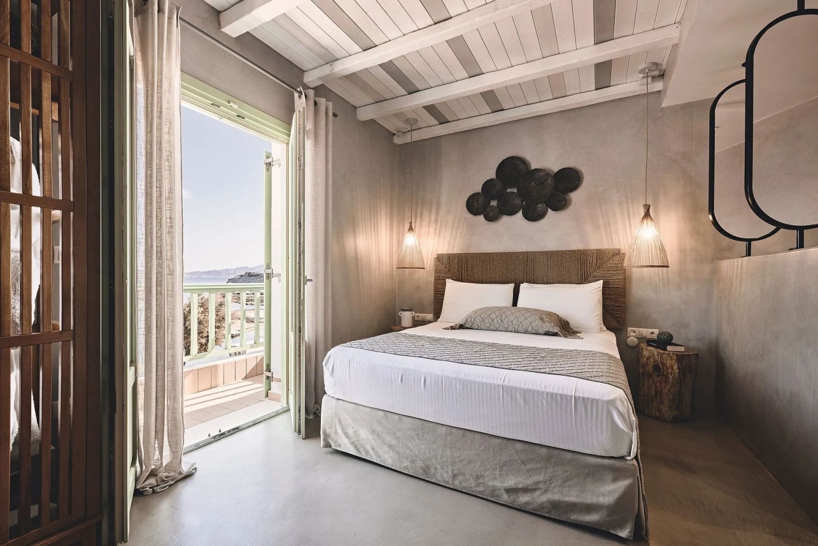 Doppelbett in einem hell gestalteten Zimmer mit Zugang zum Balkon und Holzdecke.