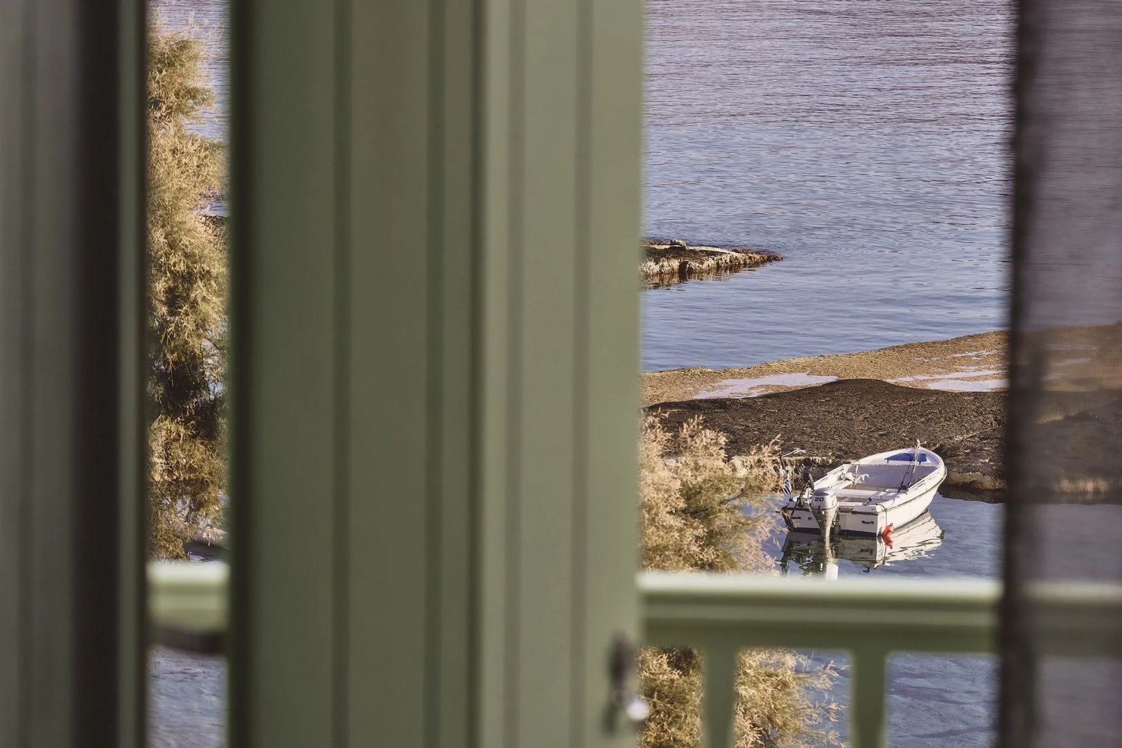 Blick von einer Terrasse auf das ruhige Meer und ein kleines Motorboot an der Küste.