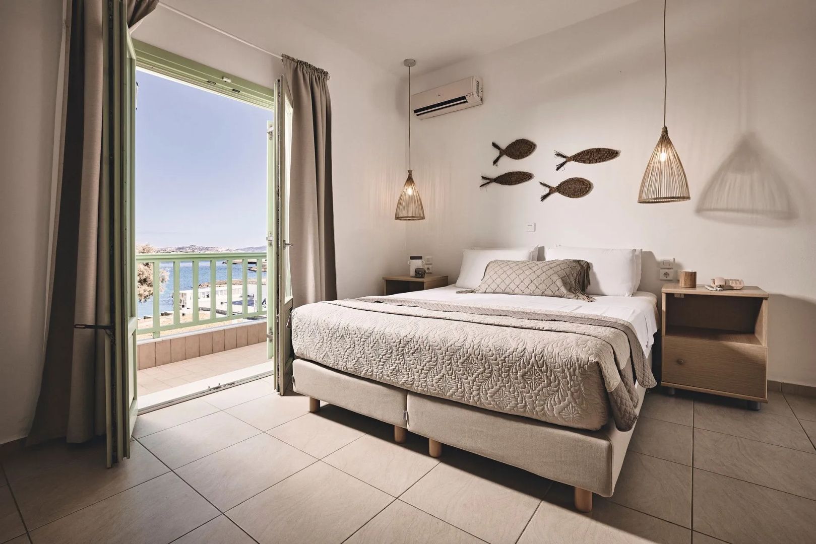 Doppelzimmer mit gemachtem Bett, Holzdeko an der Wand und Zugang zum Balkon mit Meerblick.