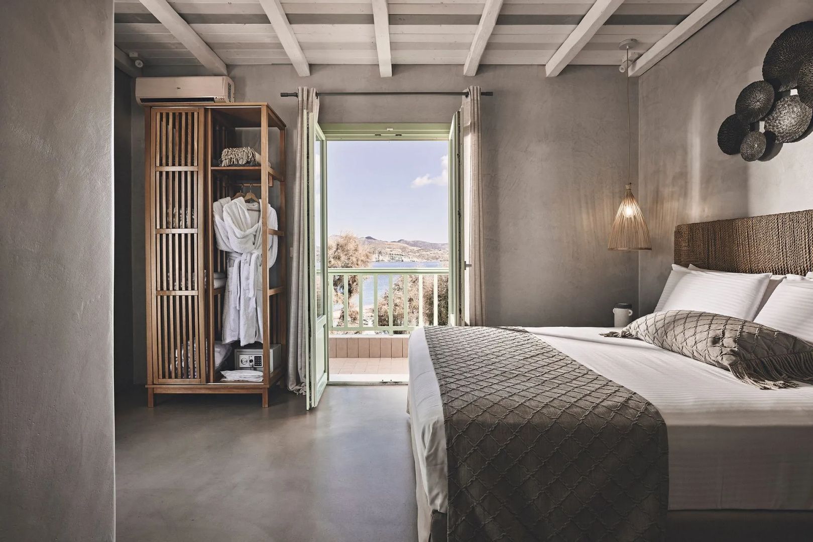 Schlafzimmer mit hellem Doppelbett, Holzschrank und Blick durch die Balkontür aufs Meer.