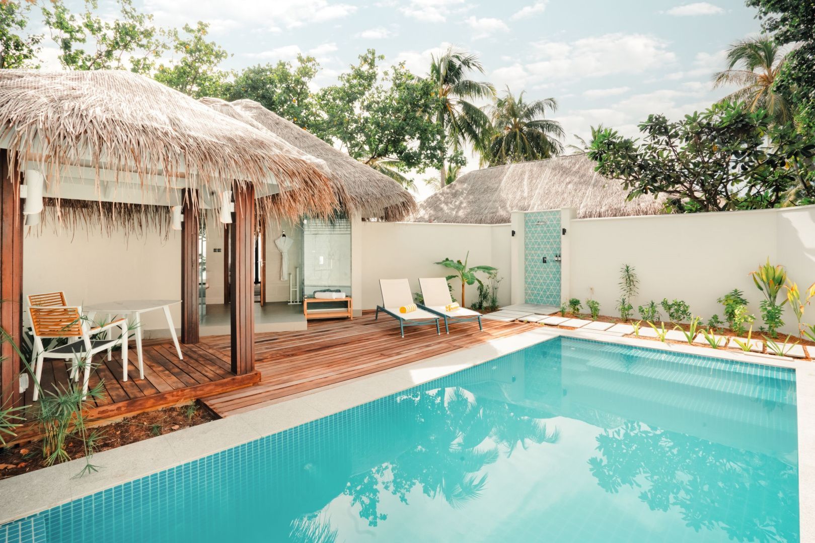 Außenbereich mit privatem Pool, Holzterrasse, zwei Sonnenliegen und reetgedecktem Bungalow.