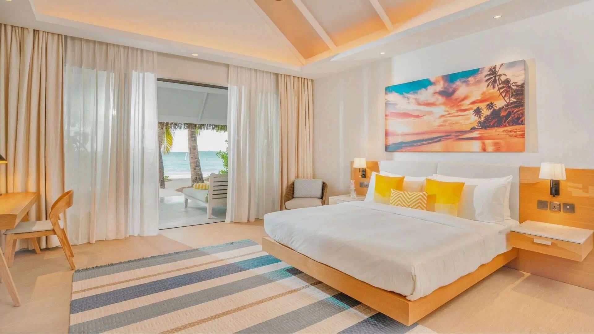 Heller Schlafraum mit großem Doppelbett, gelben Kissen und Zugang zur Terrasse mit Strandblick.
