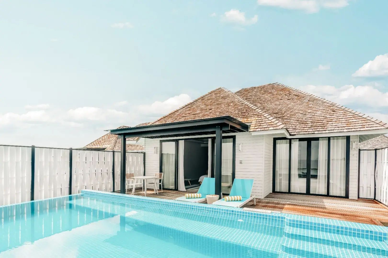 Sonnendeck einer Villa mit eigenem Pool, blauen Liegestühlen und schattiger Terrasse am Meer.
