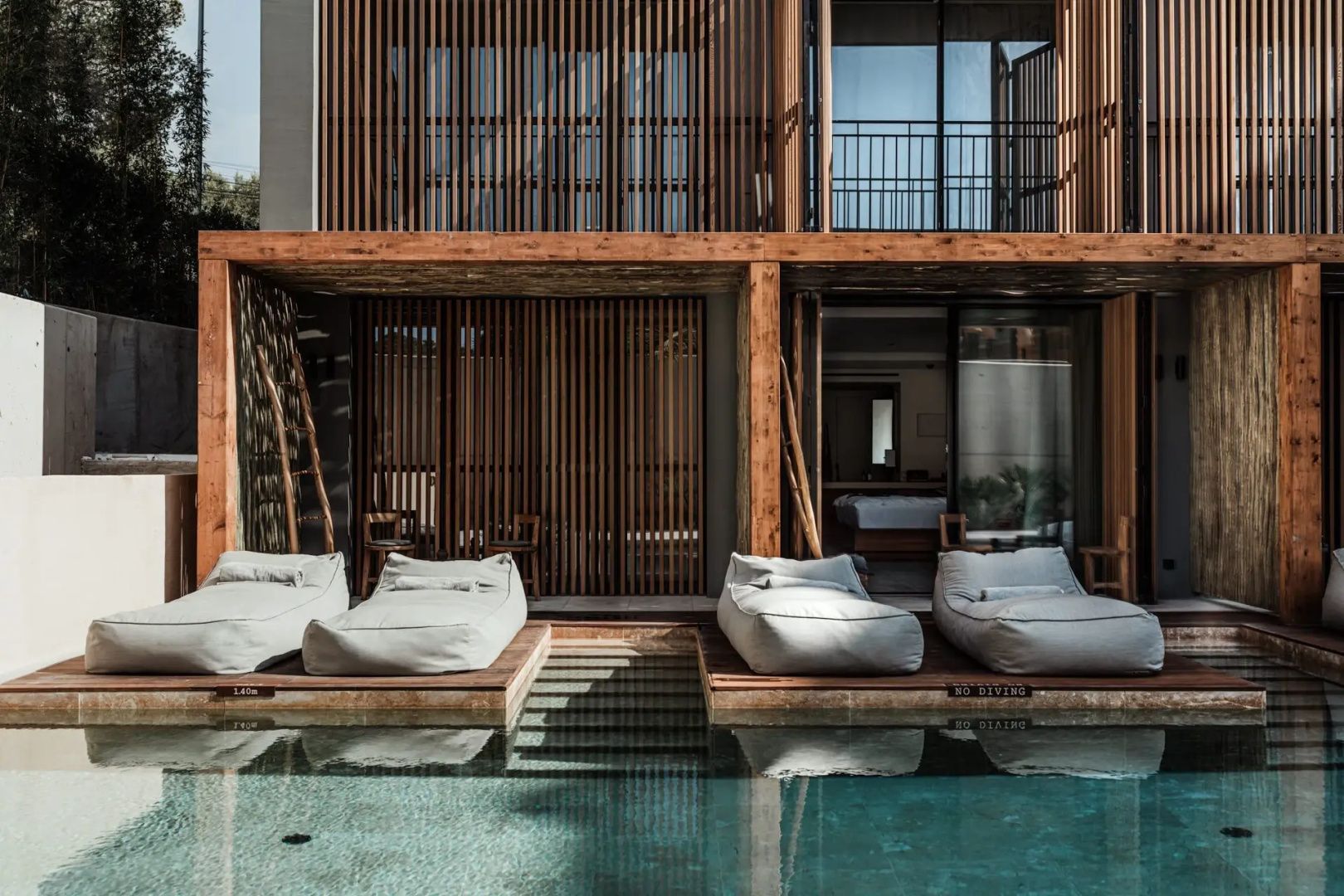 Swimup-Pool mit gepolsterten Liegekissen direkt vor der modernen Holzfassade des Gebäudes.