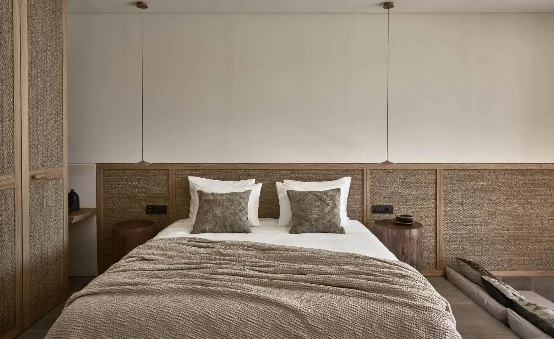 Doppelbett mit geflochtenem Kopfteil, Nachttischen aus Holz und tief hängenden Deckenleuchten.