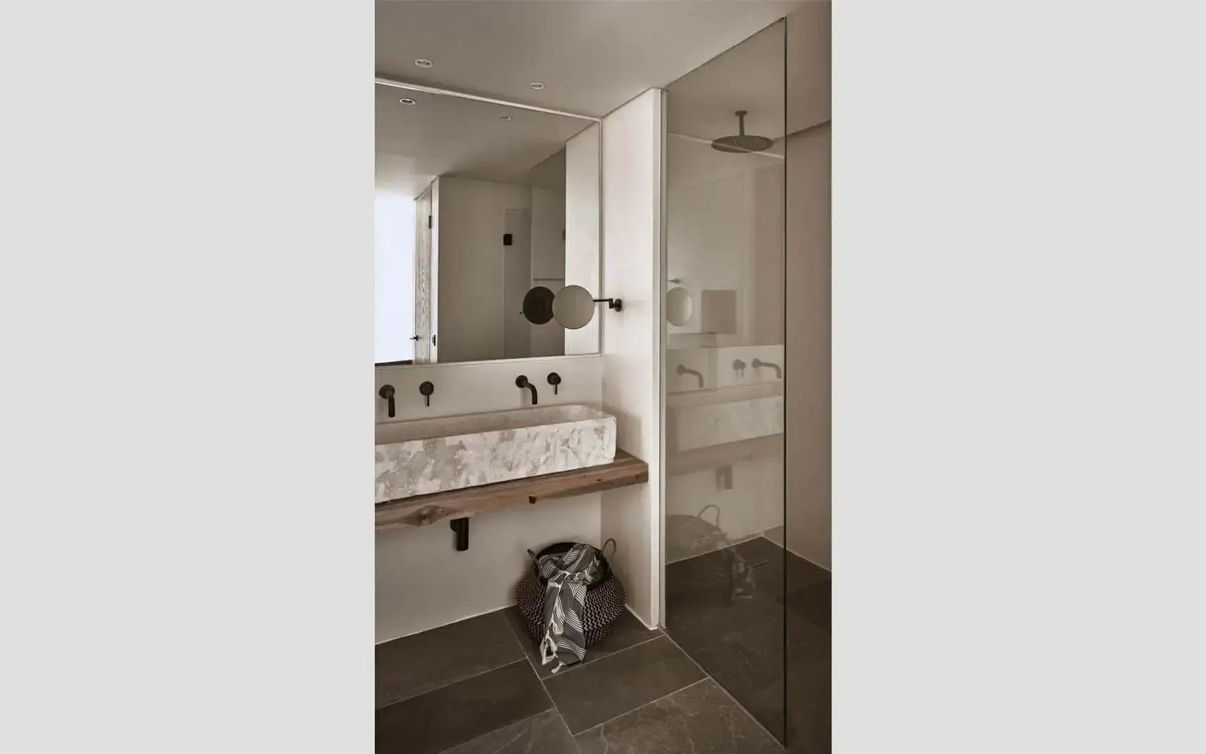 Badezimmer mit einem Waschbecken aus Stein auf einer Holzkonsole und einer ebenerdigen Glasdusche.