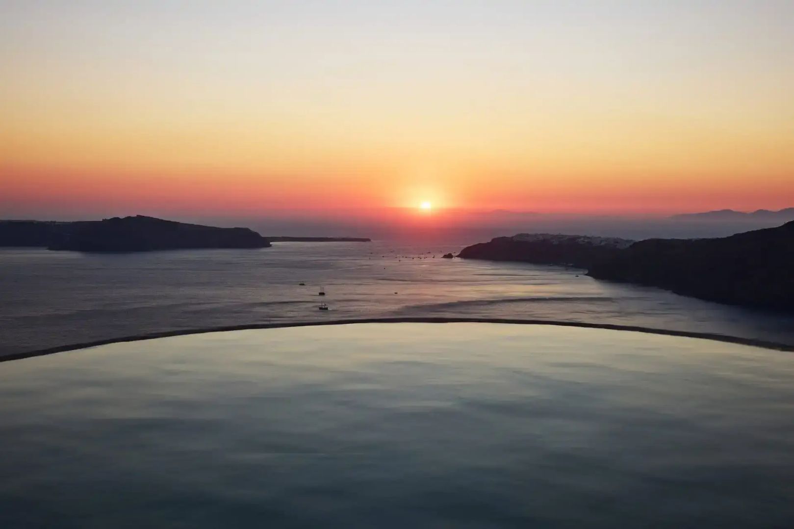 Blick über einen Infinitypool auf das Meer während des Sonnenuntergangs.