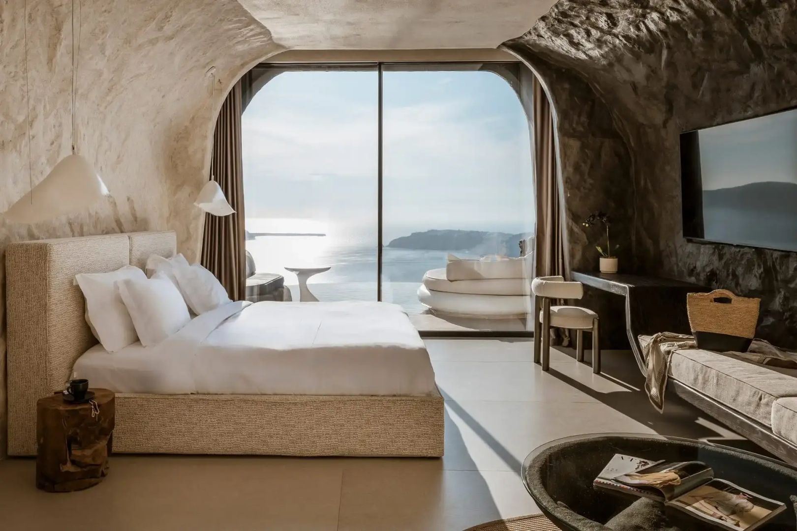 Höhlensuite mit großem Doppelbett, Schreibtisch und Glasfront mit Blick auf Meer und Terrasse.