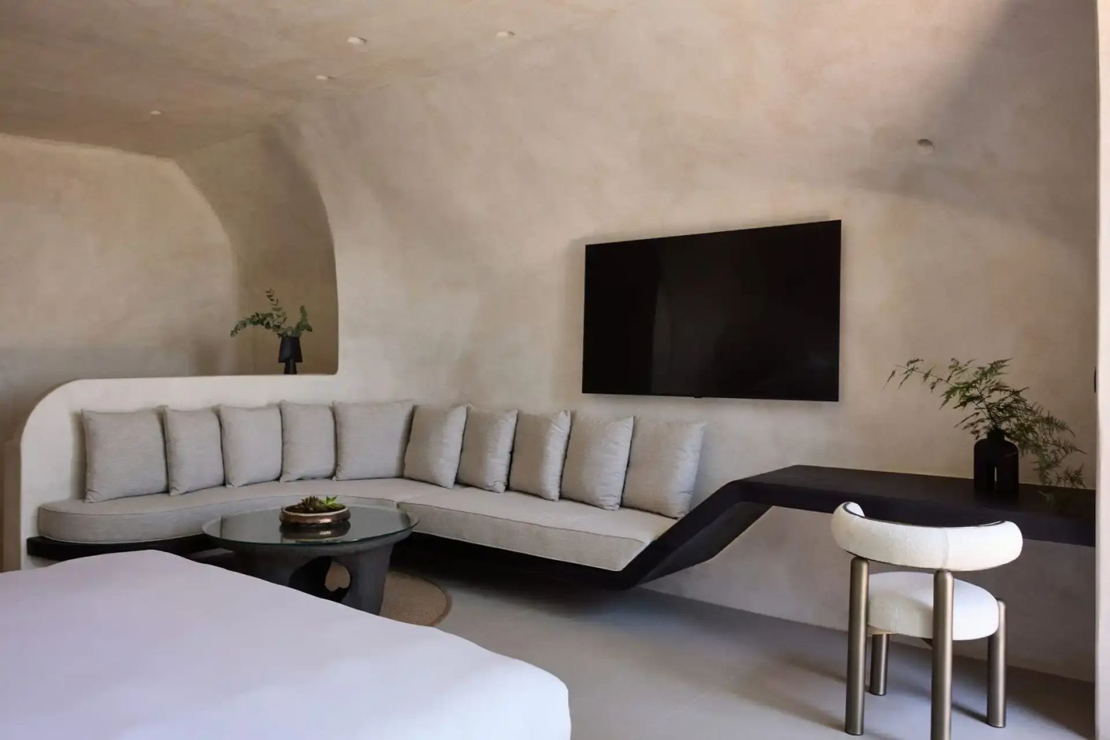 Sitzecke in einem Zimmer mit beigefarbenen Wänden, Sofa und Fernseher.