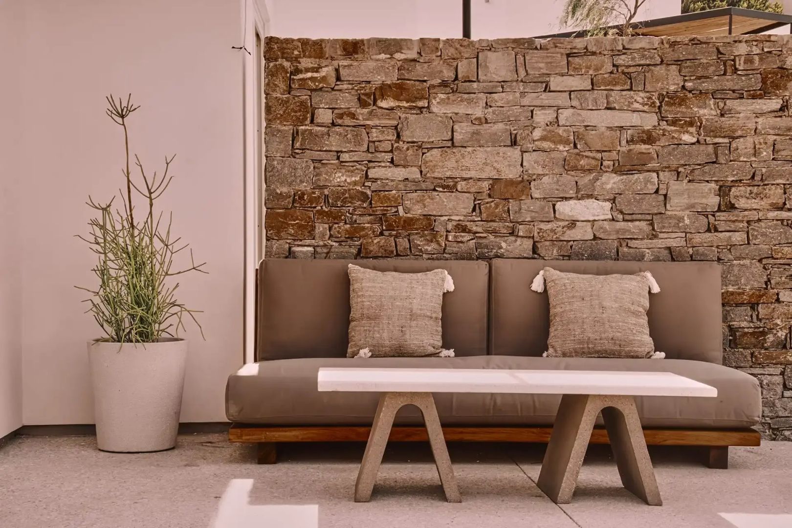 Überdachte Terrasse mit grauer Sitzbank, Kissen und einer Wand aus Naturstein.
