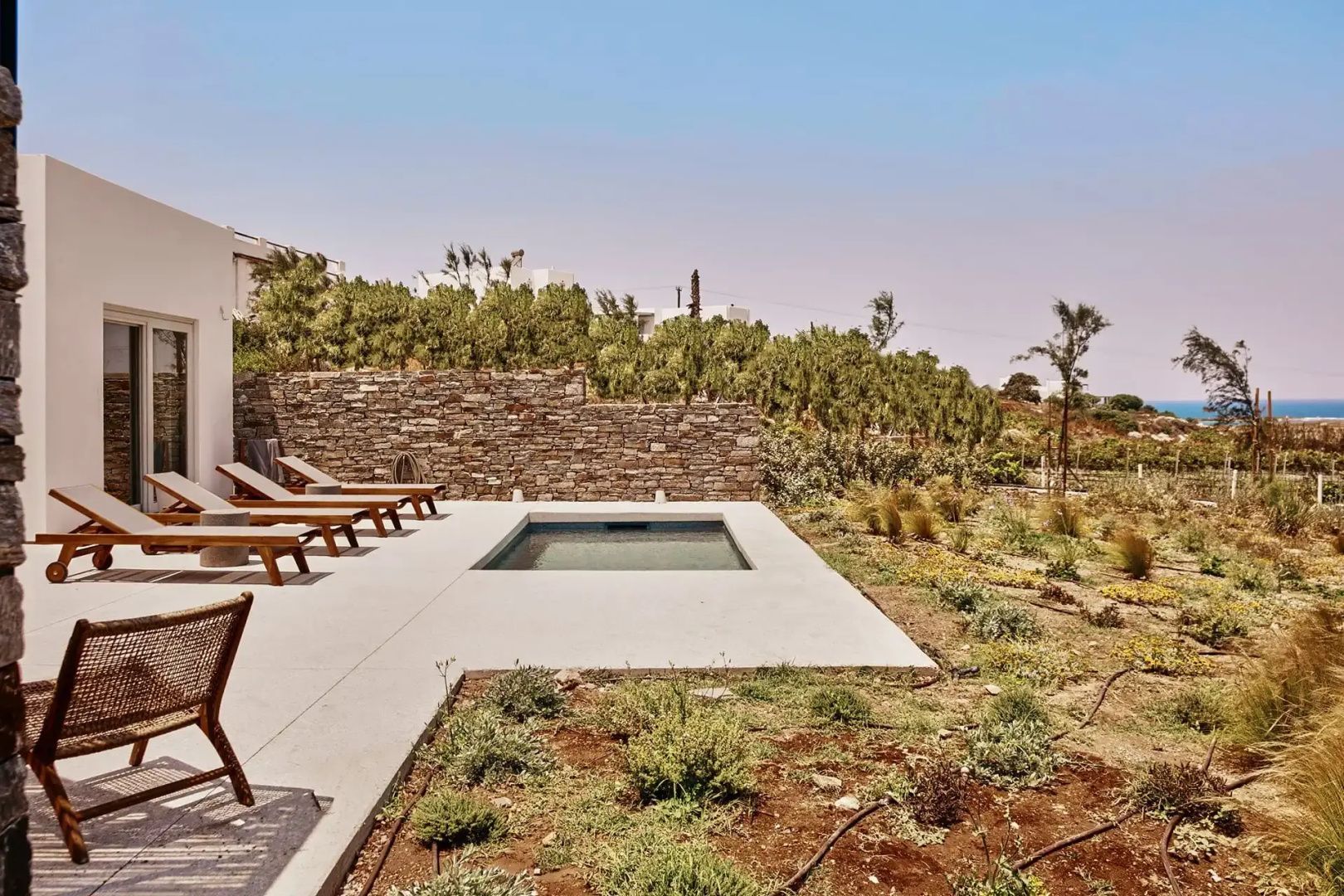 Sonnenterrasse mit kleinem Pool, Holzliegen, Steinmauer und angrenzendem Garten.