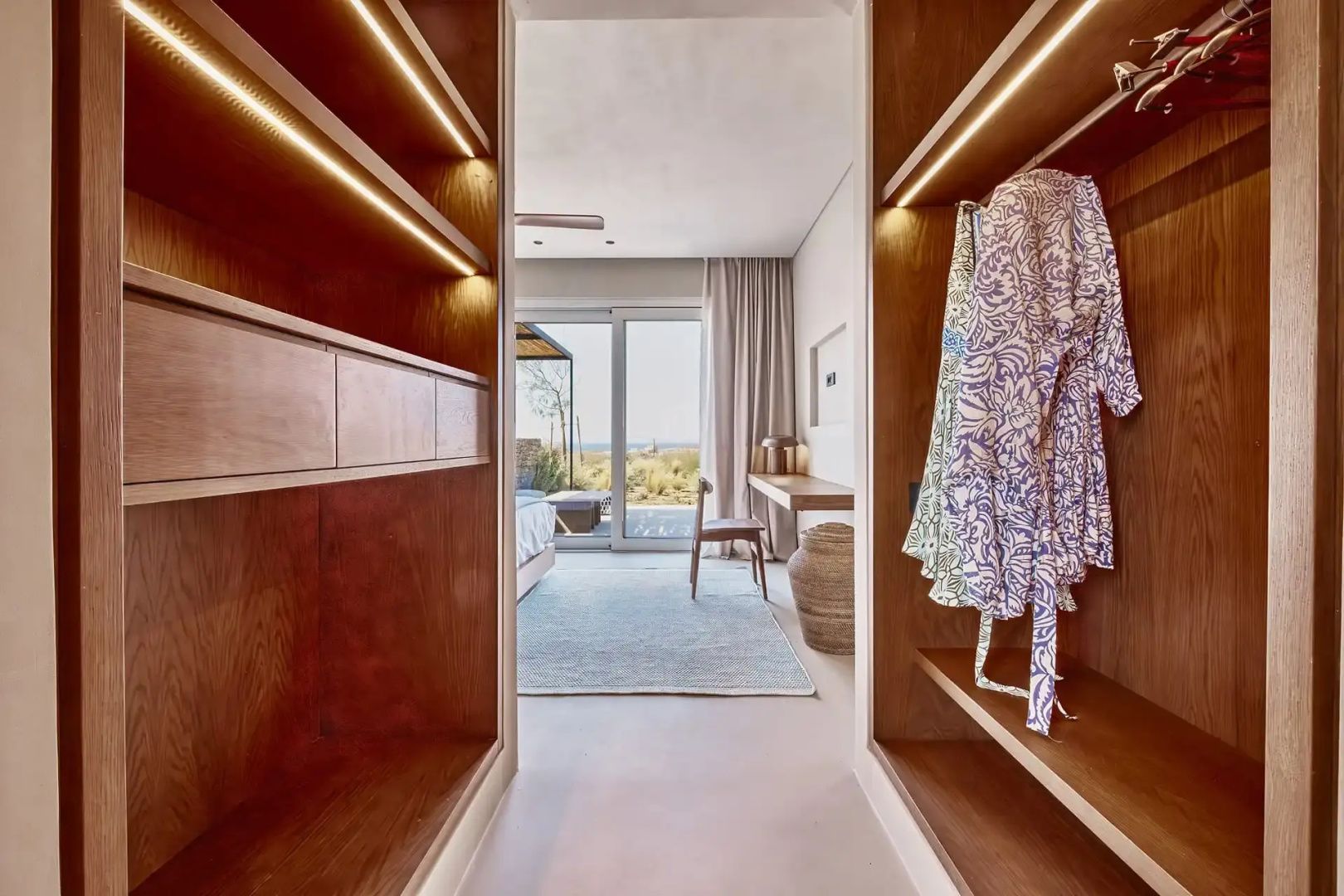 Blick durch den offenen Kleiderschrank aus Holz in das Schlafzimmer der Suite.