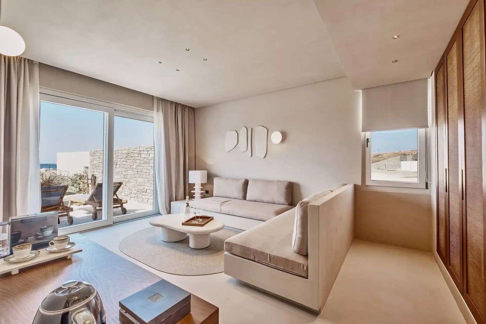 Heller Wohnbereich einer Suite mit beigefarbenen Sitzmöbeln und großer Glasschiebetür zur Terrasse.